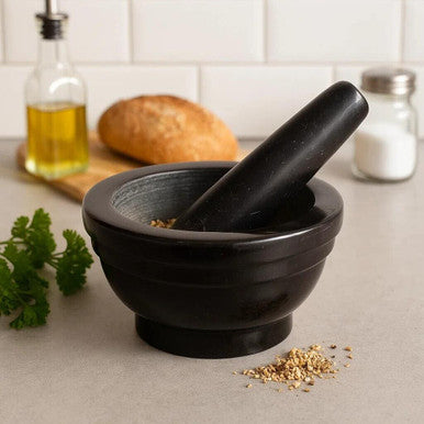 Black mortar and pestle on a kitchen counter with bread and herbs in the background