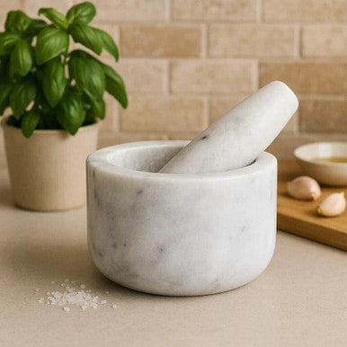 Marble mortar and pestle on a kitchen counter with a basil plant and garlic in the background.