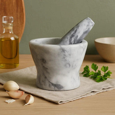 Marble mortar and pestle on a wooden table with garlic and oil in the background