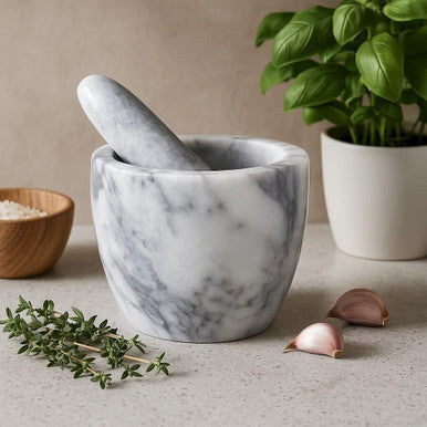 Marble mortar and pestle on a neutral surface with herbs and garlic cloves.