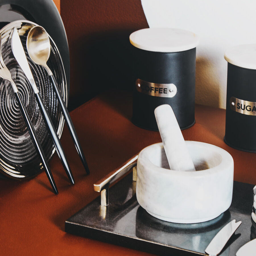 Mortar and pestle on a wooden surface with kitchen utensils and containers in the background.