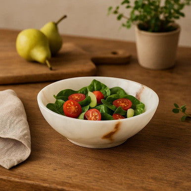 White bowl of salad with tomatoes on a wooden table with pears and a plant in the background