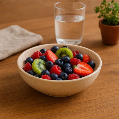 Bowl of mixed berries on a wooden table with a glass of water and plant in the background