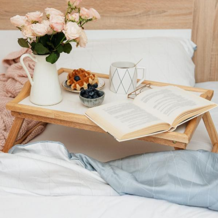 Foldable stand on a bed with a book, mug, and flowers
