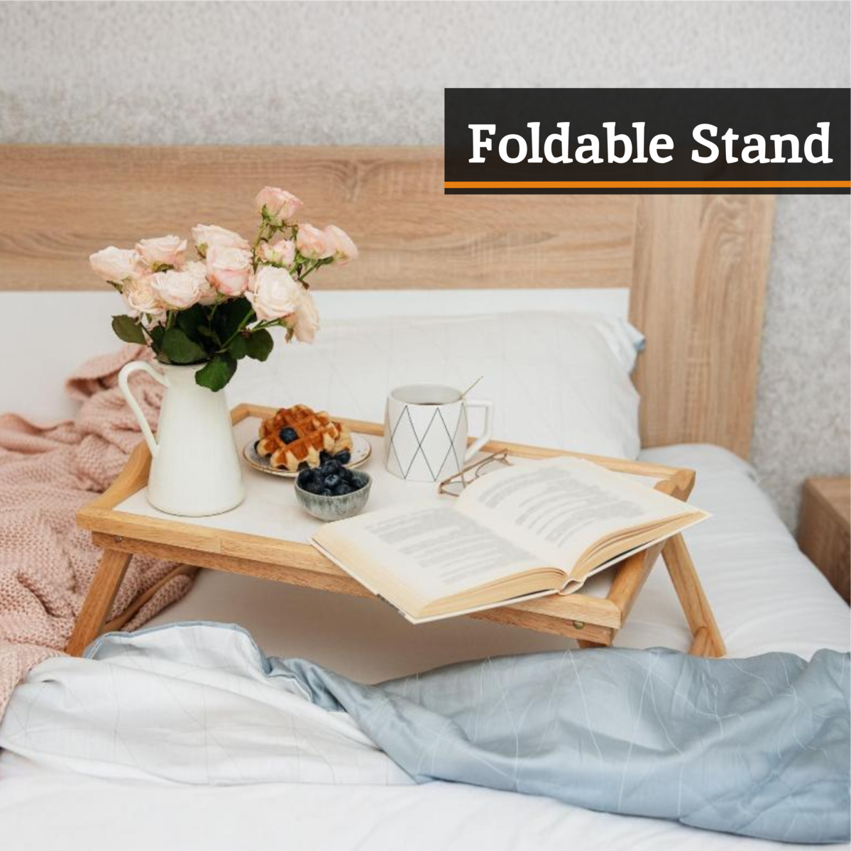 Foldable stand on a bed with a book, mug, and flowers