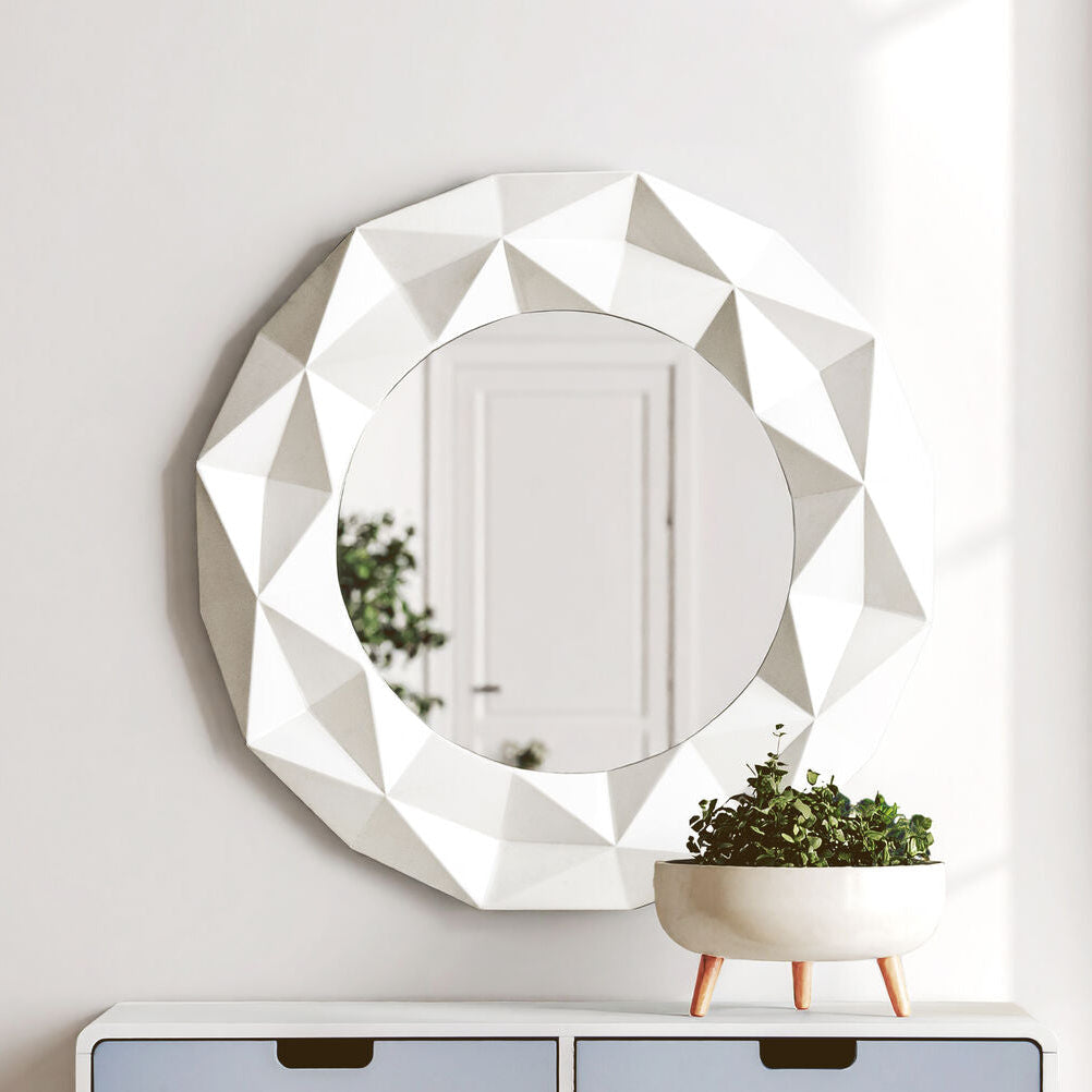 Decorative wall mirror with geometric design above a small table with drawers and a plant.