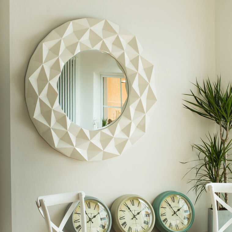Decorative mirror with geometric design above a console table with decorative clocks and chairs.