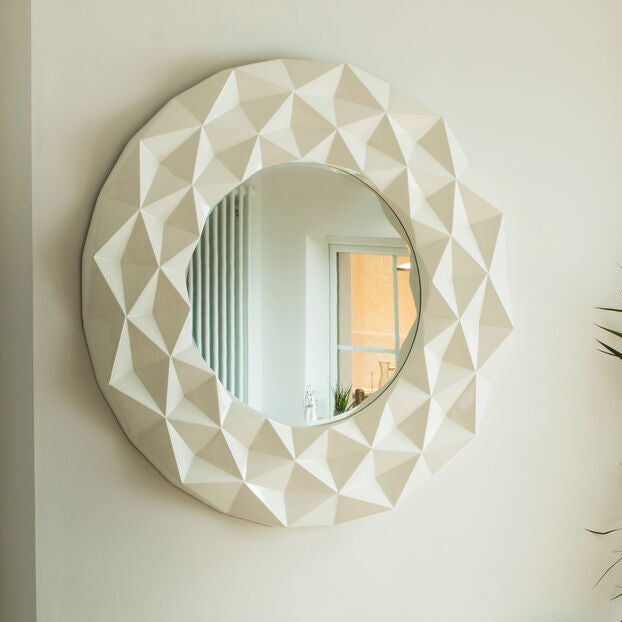 Decorative mirror with geometric design above a console table with decorative clocks and chairs.