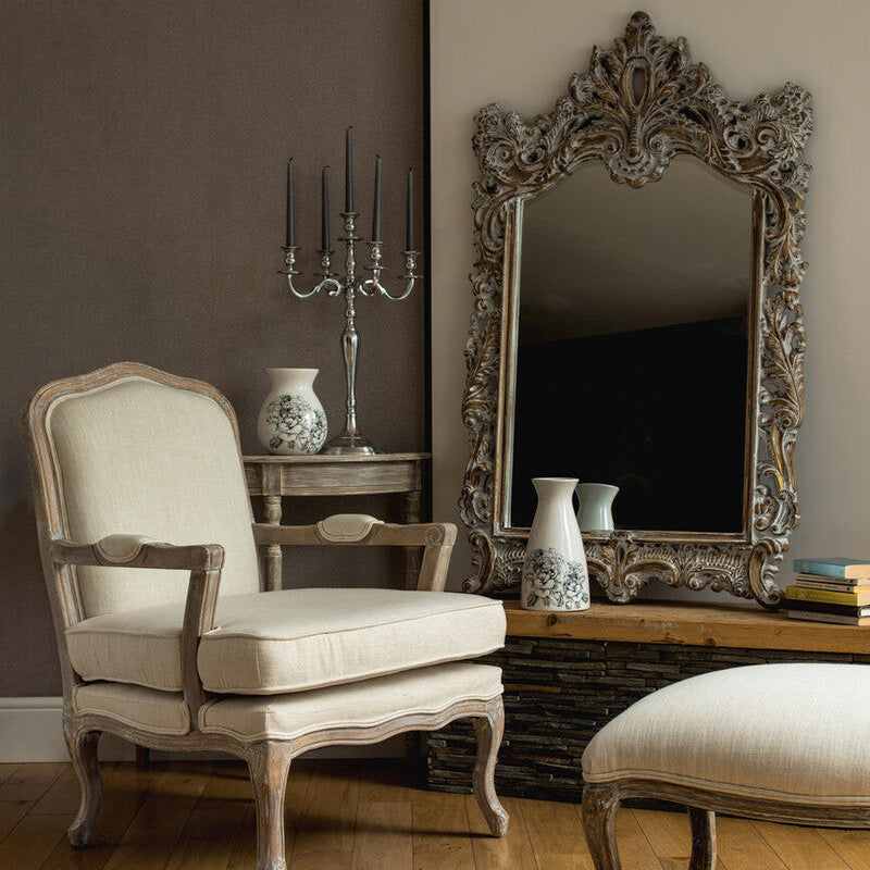 Living room with ornate mirror, chair, and ottoman on wooden floor.