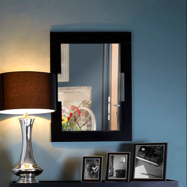 Decorative shelf with a lamp, mirror, and framed pictures against a blue wall.