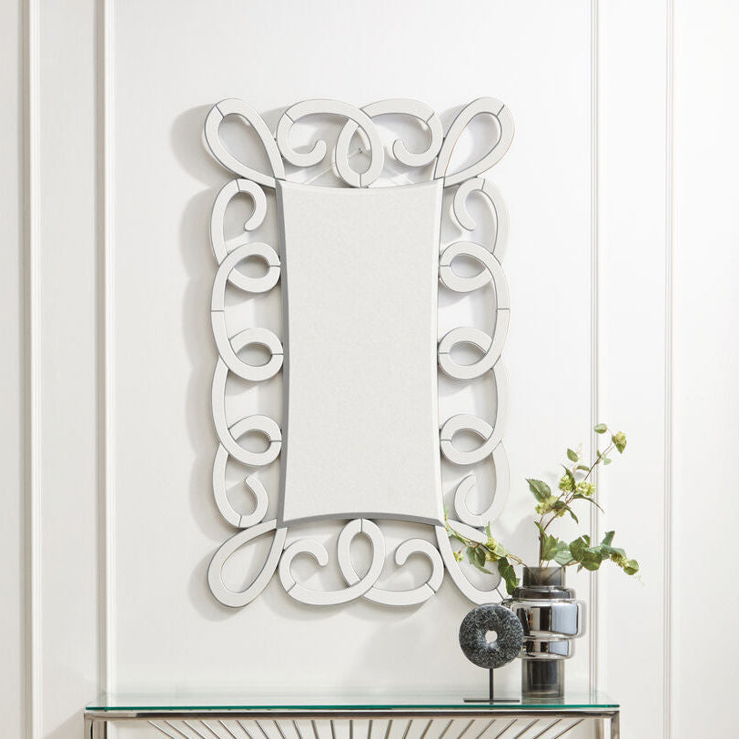 Decorative wall mirror with intricate white frame on a light-colored wall.