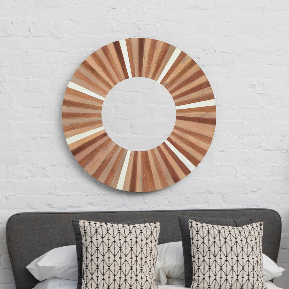Wooden circular mirror on a white brick wall above a bed with patterned pillows.
