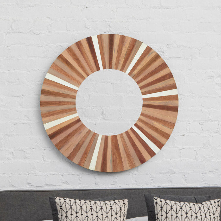 Wooden circular mirror on a white brick wall above a bed with patterned pillows.