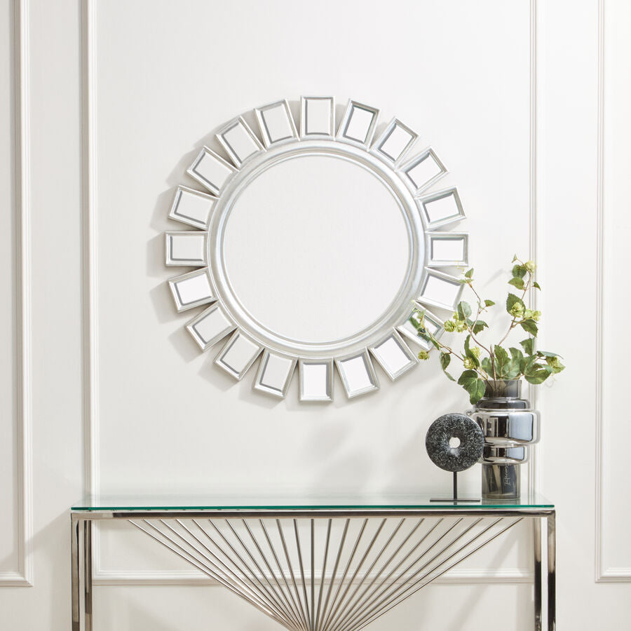 Decorative wall mirror with a glass console table below on a white wall.