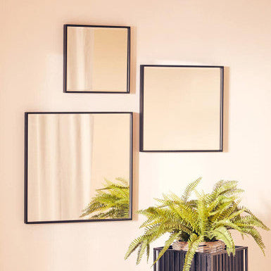Three square mirrors with black frames on a beige wall, with a potted fern in the foreground.