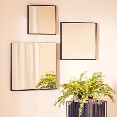 Three square mirrors with black frames on a beige wall, with a potted fern in the foreground.