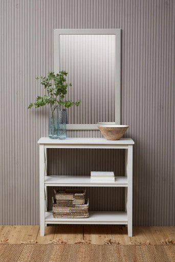 White cabinet with a mirror, plant, and bowls against a striped wall.