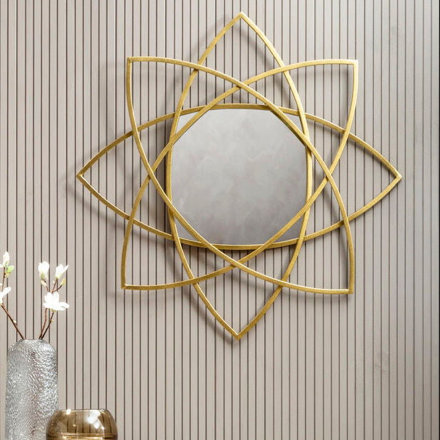 Decorative wall mirror with geometric design on a striped wall with a vase and flowers on a pedestal.