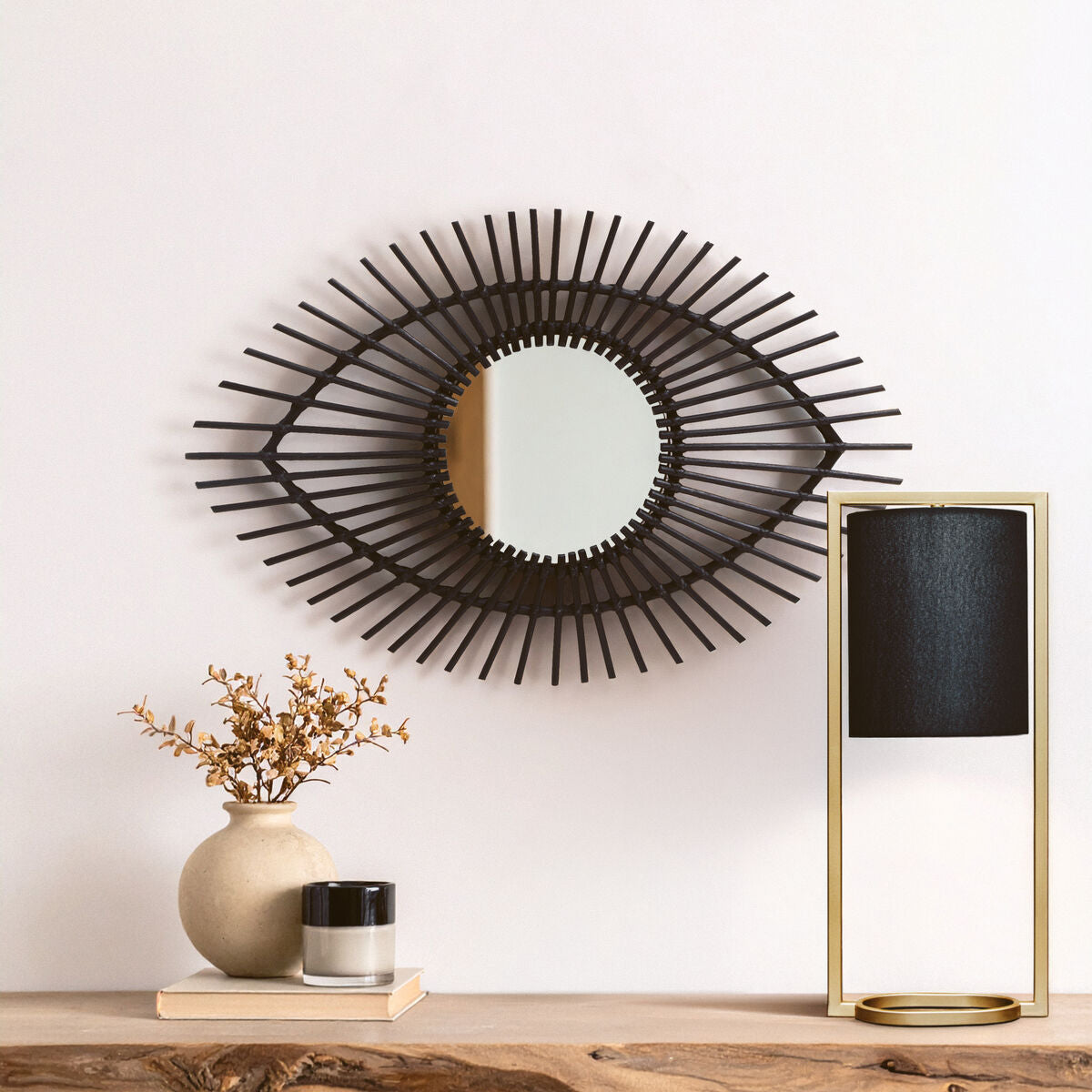 Decorative wall mirror with a modern design on a white wall above a wooden shelf with decorative items.