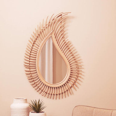 Decorative wall mirror with wicker-like frame on a beige wall above a small table with a vase and plant.