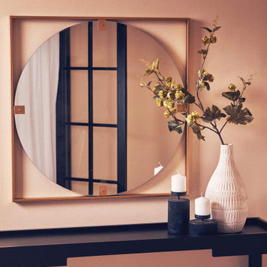 Round mirror with wooden frame on a wall above a console table with decorative items.