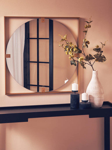 Round mirror with wooden frame on a wall above a console table with decorative items.