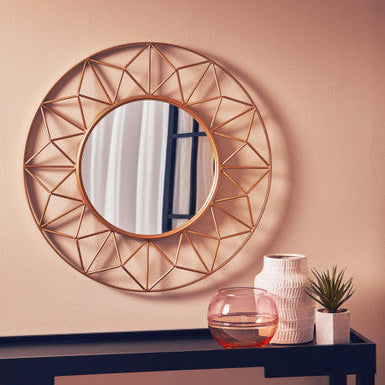 Round decorative mirror with geometric frame on a wall above a console table with decor items.