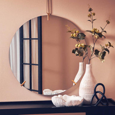 Round mirror on a wall with decorative items including a vase and flowers.