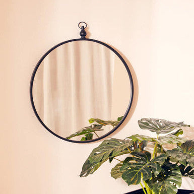 Round mirror with black frame on a beige wall next to a potted plant