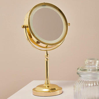 Gold vanity mirror on a white surface with a beige background