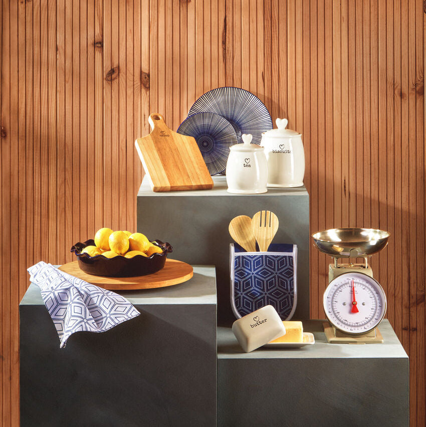 Kitchen counter with various items including a bowl of lemons, a scale, and utensils against a wooden wall.