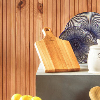 Kitchen counter with various items including a cutting board, lemons, a scale, and utensils against a wooden wall.