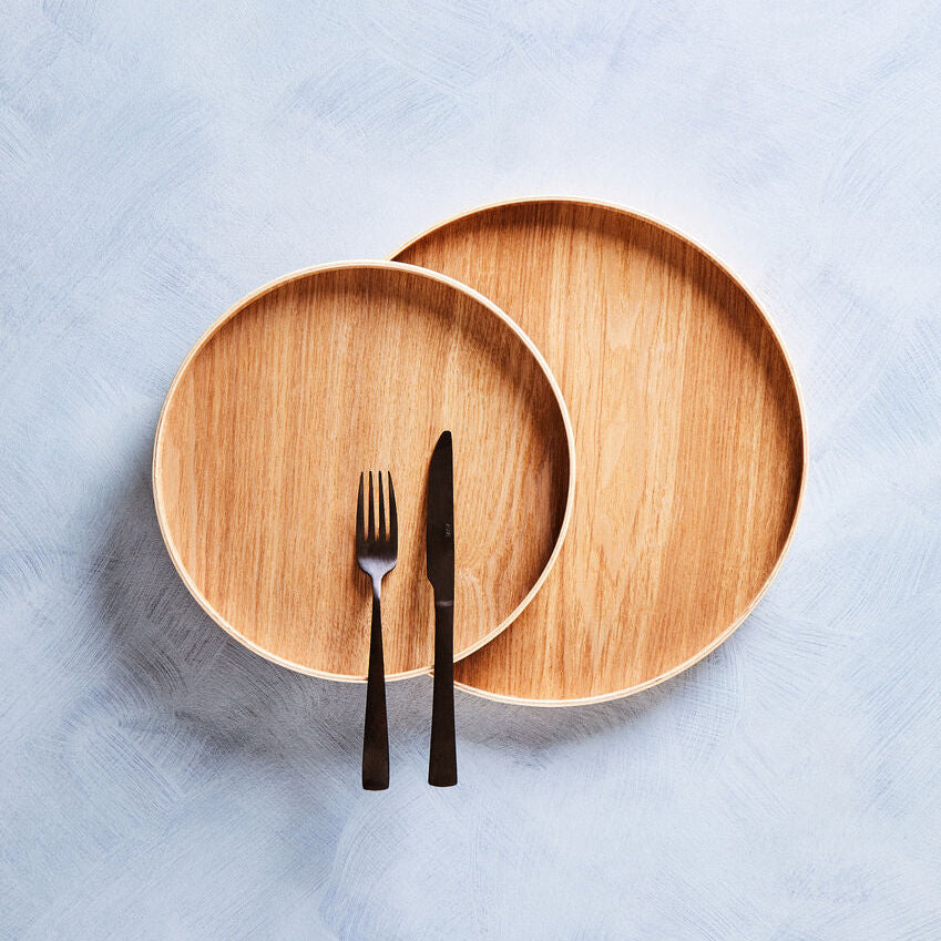 Two wooden plates with a fork and knife on a light blue textured surface