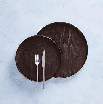 Two dark wooden plates with a fork and knife on a light blue background
