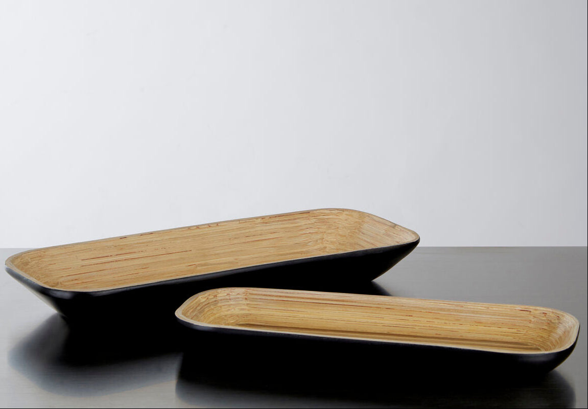 Two rectangular ceramic trays, one black and one brown, on a reflective surface with a light gray background.