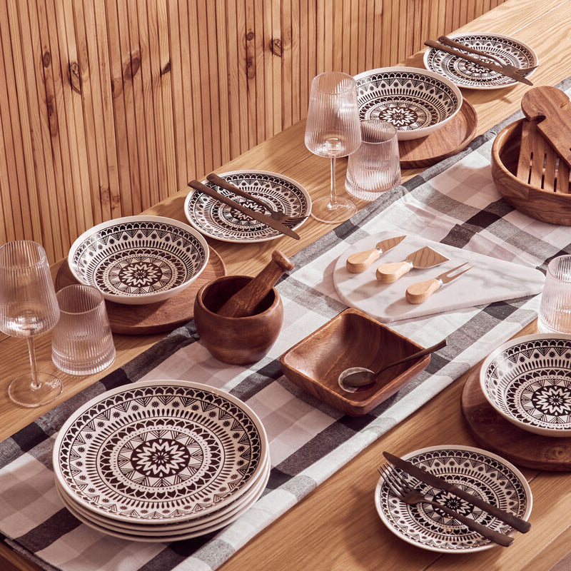 Dining table set with ceramic plates, wooden bowls, and cutlery on a checkered tablecloth.