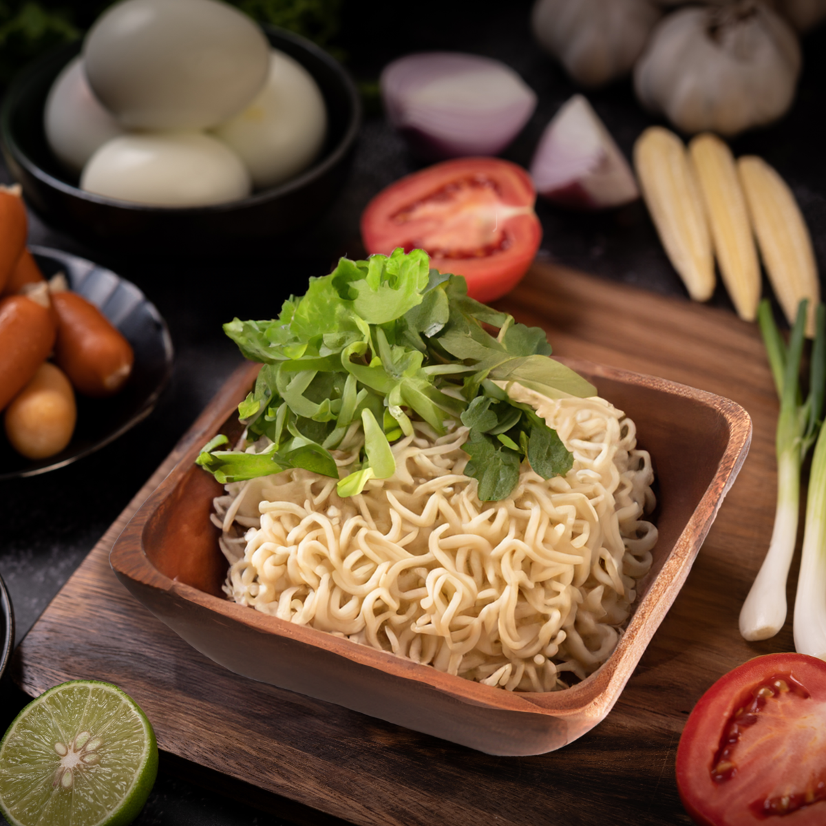 Noodles with greens in a wooden bowl on a dark surface with ingredients around
