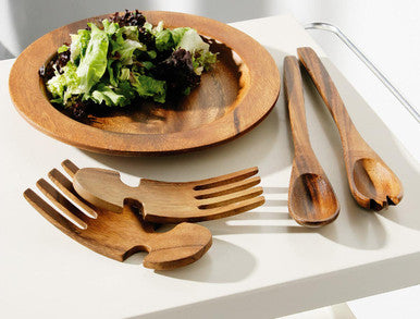 Wooden salad bowl with salad and matching wooden utensils on a white surface