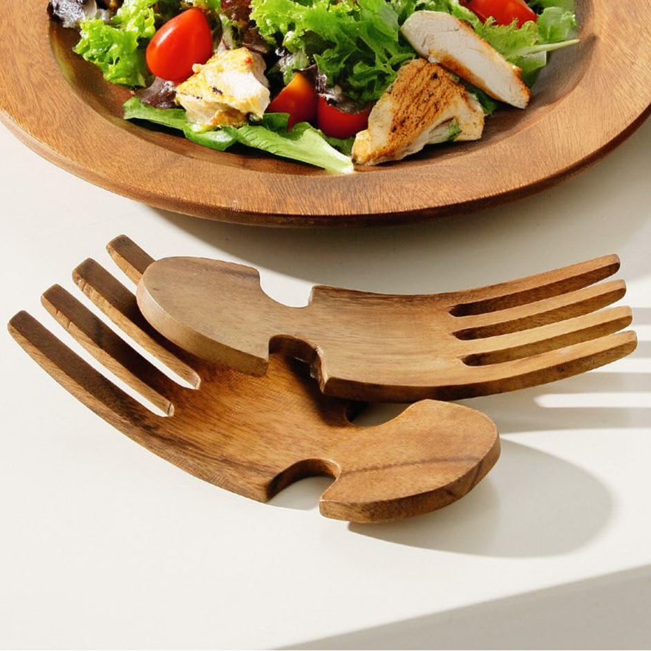 Wooden salad server set with a plate of salad on a white surface
