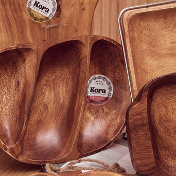 Wooden cutting board and trays with Kora branding on a wooden surface.