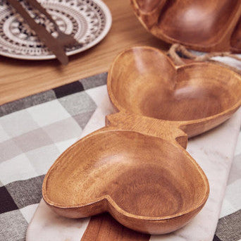Wooden heart-shaped bowl on a checkered tablecloth with a marble coaster underneath.