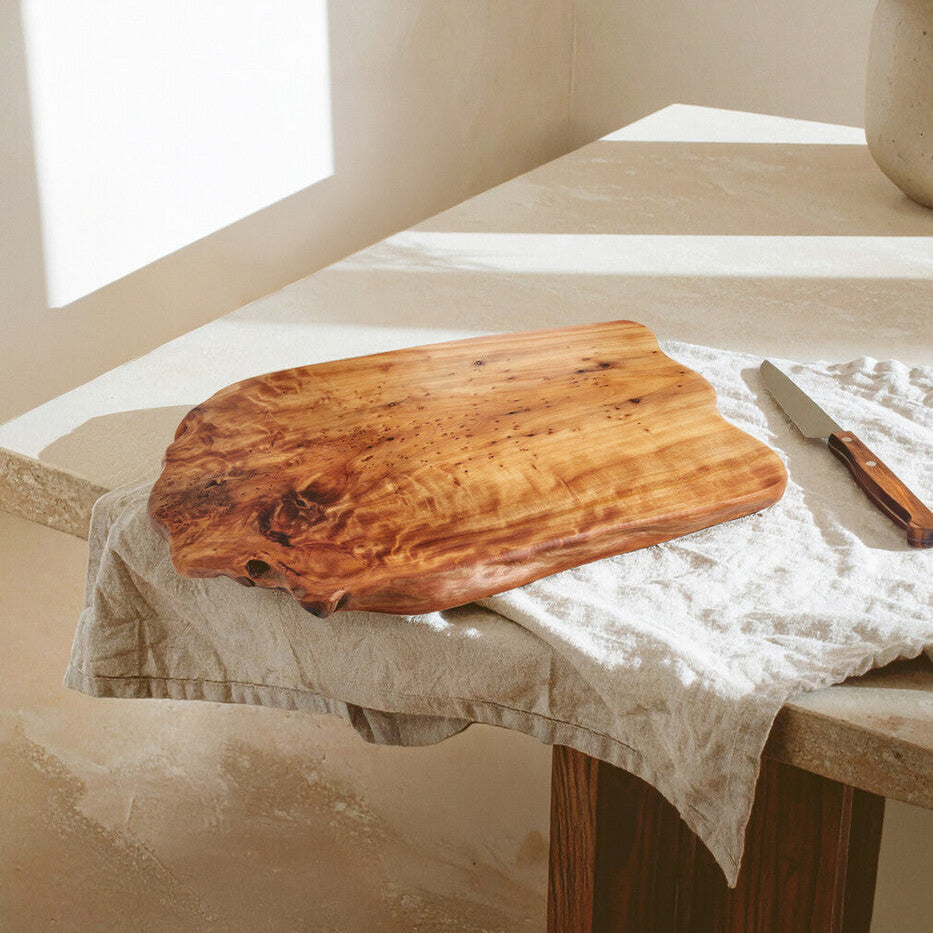 Wooden cutting board on a table with a knife and plant in the background