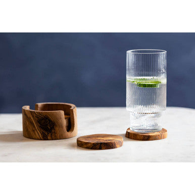 Clear glass with water and a lime on a wooden coaster, with a wooden bowl and coaster in the foreground.