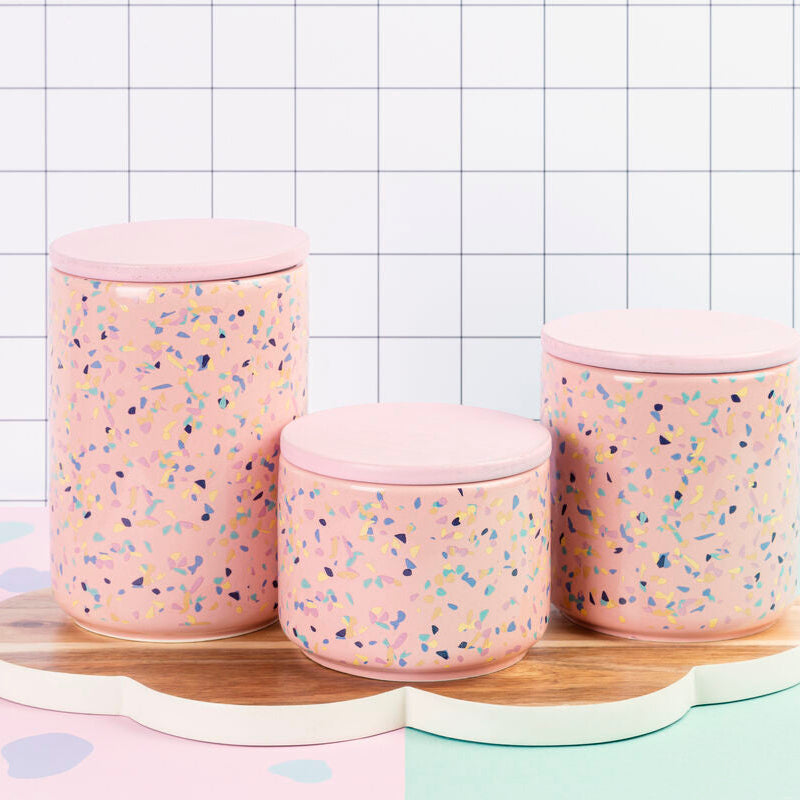 Three pink textured jars with a wooden tray on a checkered background