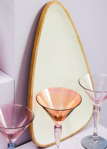 Three colorful glassware items on a white surface with a light green mirror in the background.