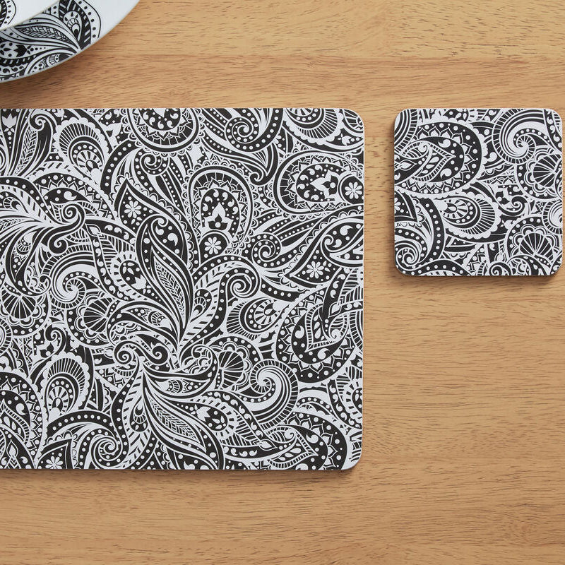 Black and white paisley patterned placemat and coaster on a wooden table.