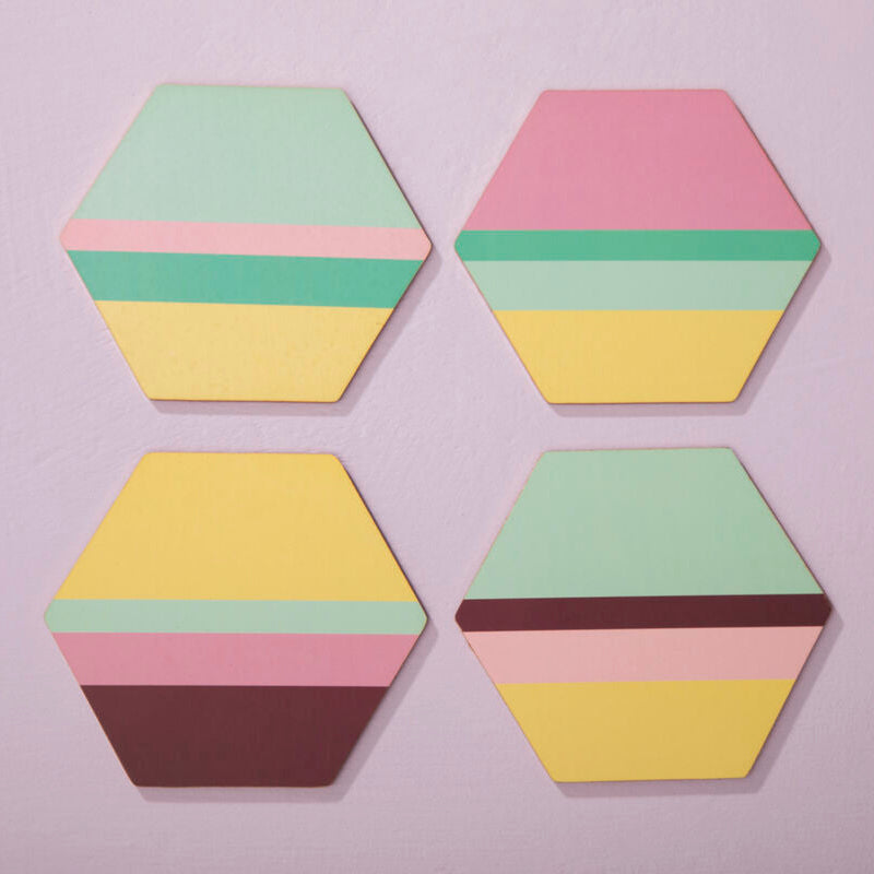 Four hexagonal coasters with multicolored layers on a light purple background
