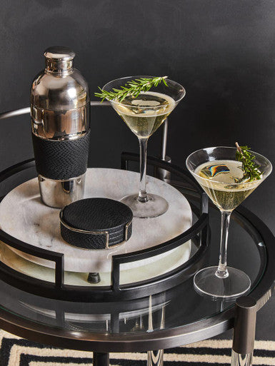 Cocktail shaker and two cocktails on a round tray with a dark background