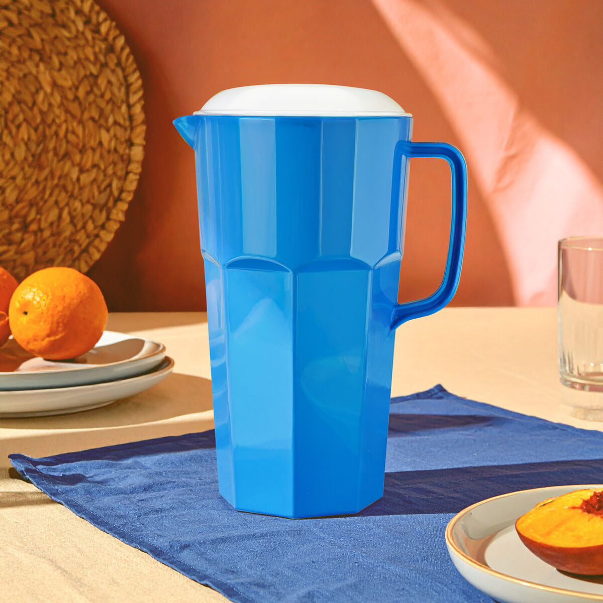 Blue pitcher on a table with plates of fruit and a blue placemat.