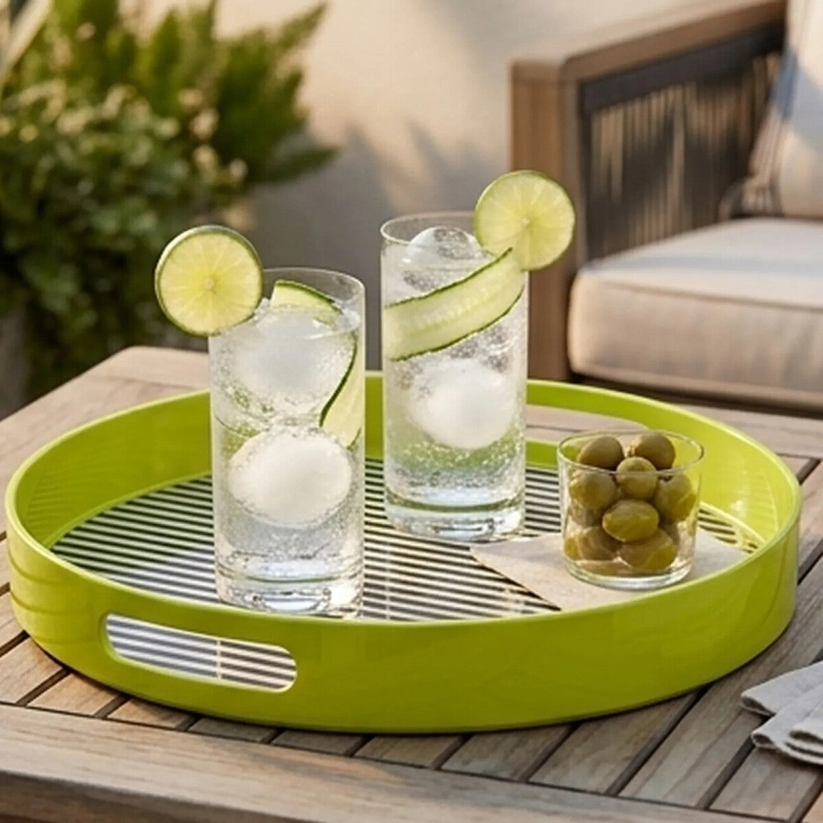 Green tray with two glasses of water, lime slices, and a small glass of green olives on a wooden table outdoors.